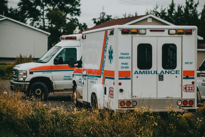 Two ambulances parked one east/west and one parked behind it going north/south with taller grass along the back side of them. Looks like a more rural setting.